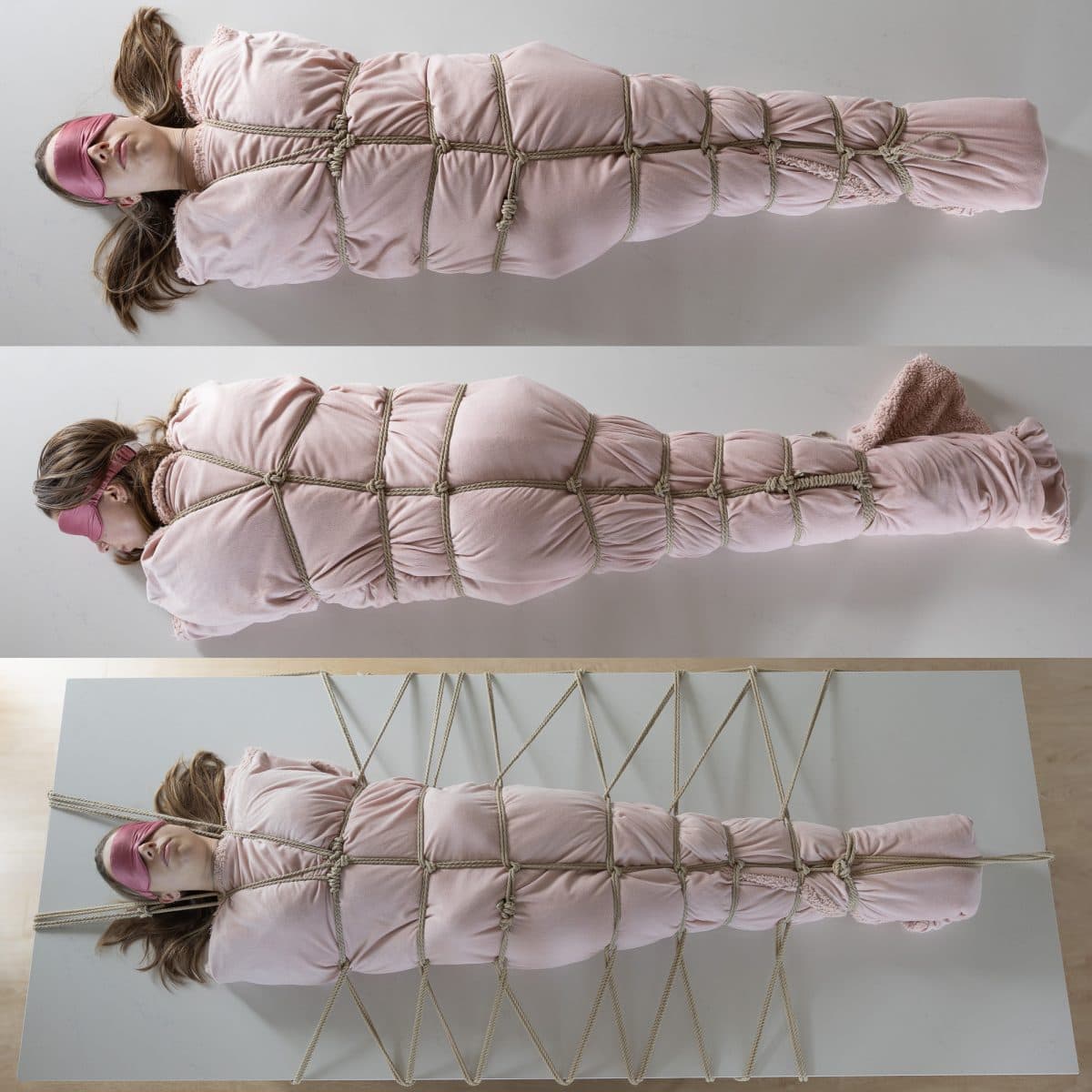 이 사진은 한 젊은 여성이 푹신한 분홍색 담요에 단단히 싸여 있는 모습을 보여줍니다. 담요를 몇 인치 간격으로 감싸고 있는 끈이 담요를 닫아 고정하고 있습니다. 누에고치는 주방 카운터 위에 놓여 있고, 더 많은 밧줄이 누에고치에서 방사형으로 바깥쪽으로 뻗어 카운터 바깥쪽에 부착되어 여성을 카운터 중앙에 움직이지 않게 고정하고 있습니다.