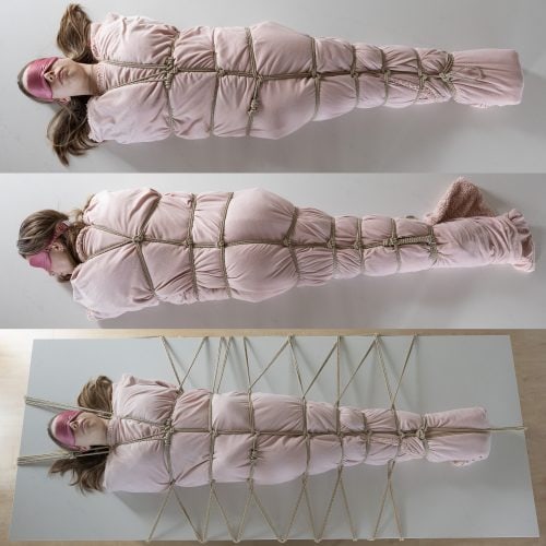 This picture shows a young woman wrapped tightly in a fuzzy pink blanket. There are straps of rope wrapped around that blanket every few inches to hold it closed. The cocoon is resting on top of a kitchen counter and more ropes run radially outward from the cocoon and are attached around the outside of the counter, affixing the woman immovably to the center of the counter.
