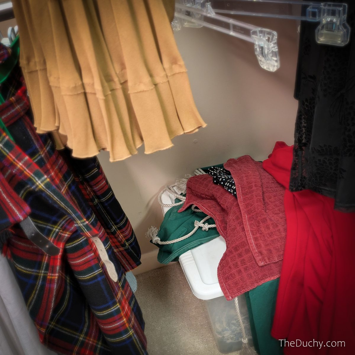 A photo of a closet floor. Skirts and hangers of varying colors and textures frame a white box. A pile of clothing sits on top of the box, the ends of twisted linen hemp ropes can be seen peeking though.
